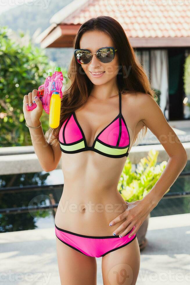 bonito Delgado mujer jugando con pistola de agua juguete a piscina en verano tropical vacaciones foto