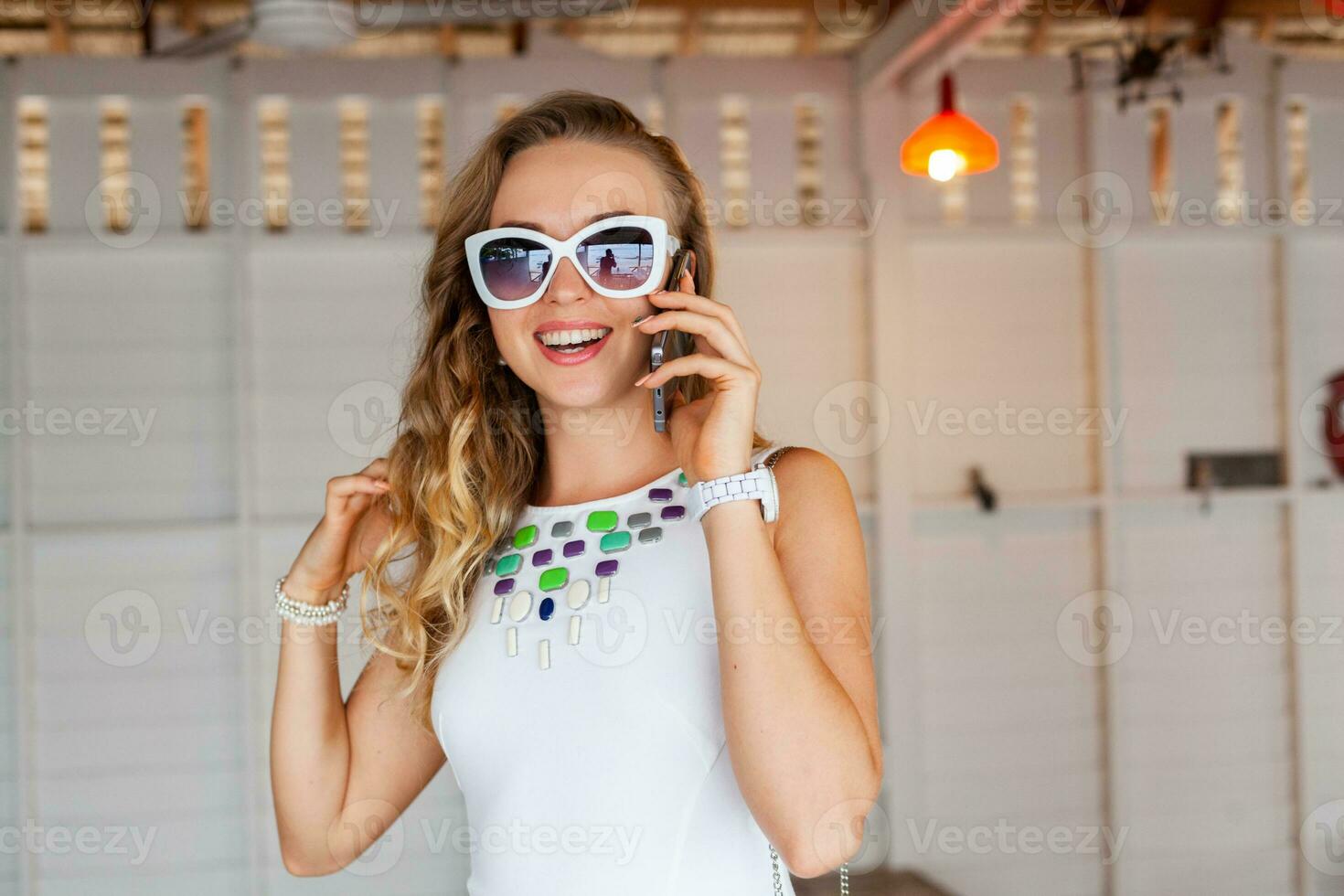 attractive woman in white dress in summer cafe in sunglasses talking on phone photo