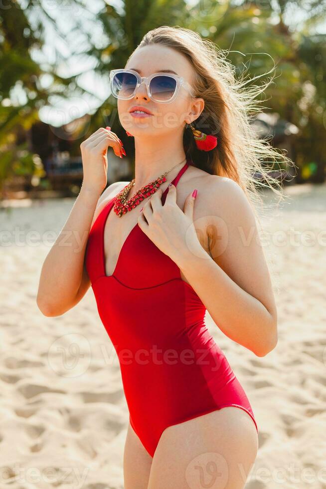 young beautiful blond woman sunbathing on beach in red swimming suit, sunglasses photo