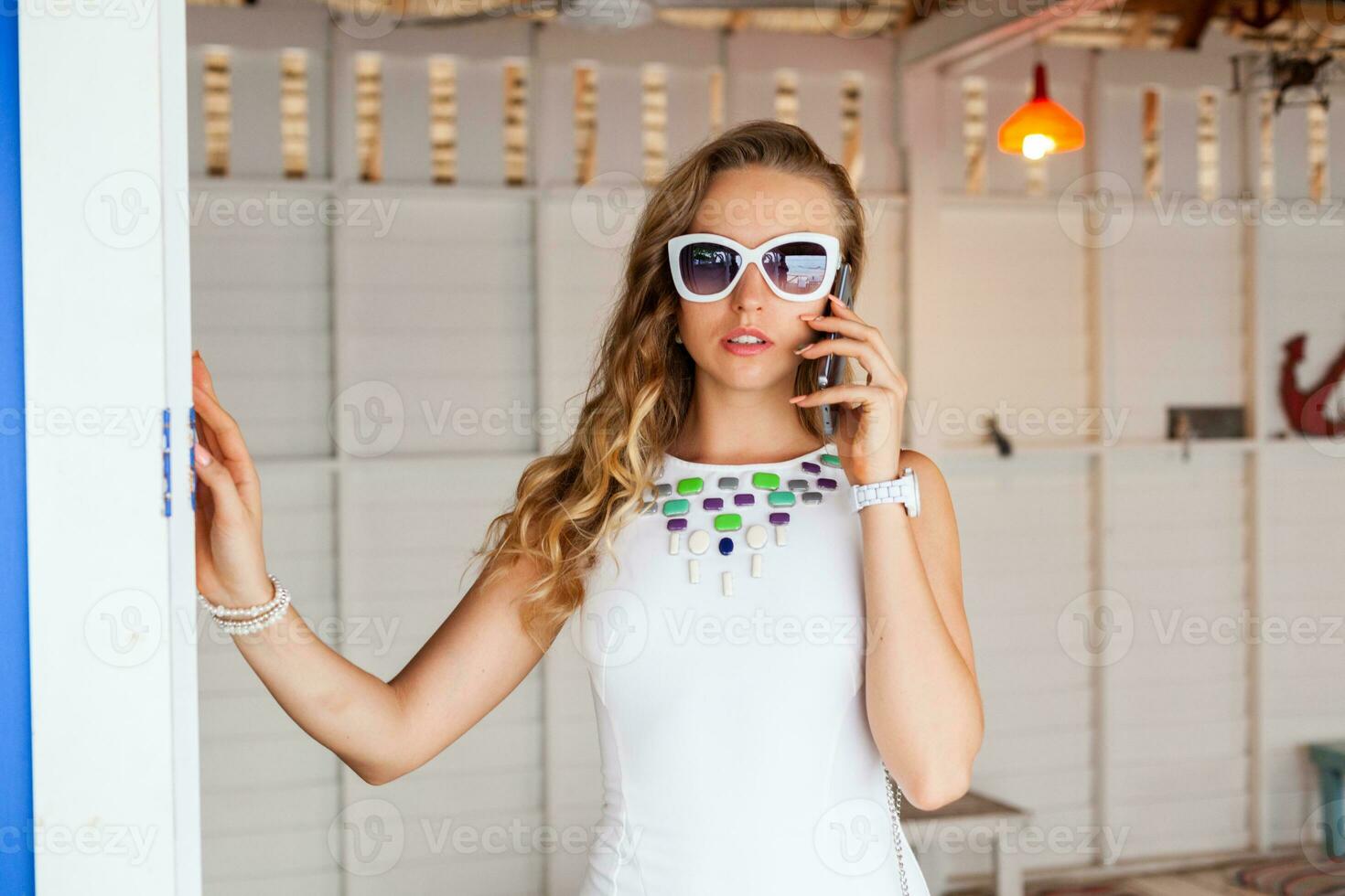 attractive woman in white dress in summer cafe in sunglasses talking on phone photo