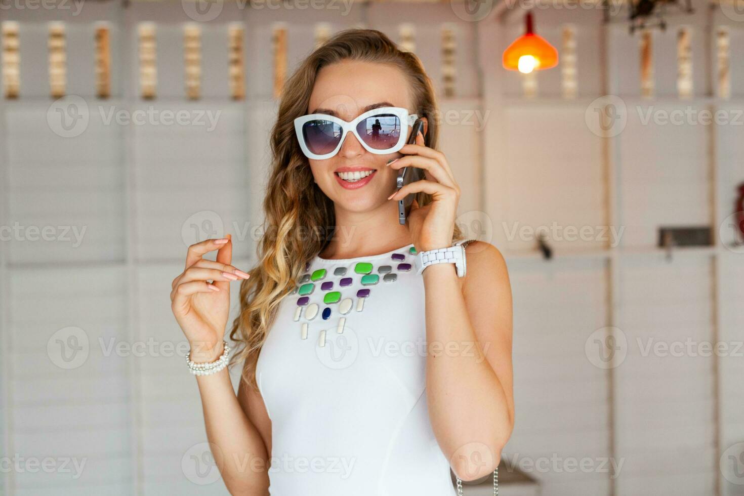 attractive woman in white dress in summer cafe in sunglasses talking on phone photo