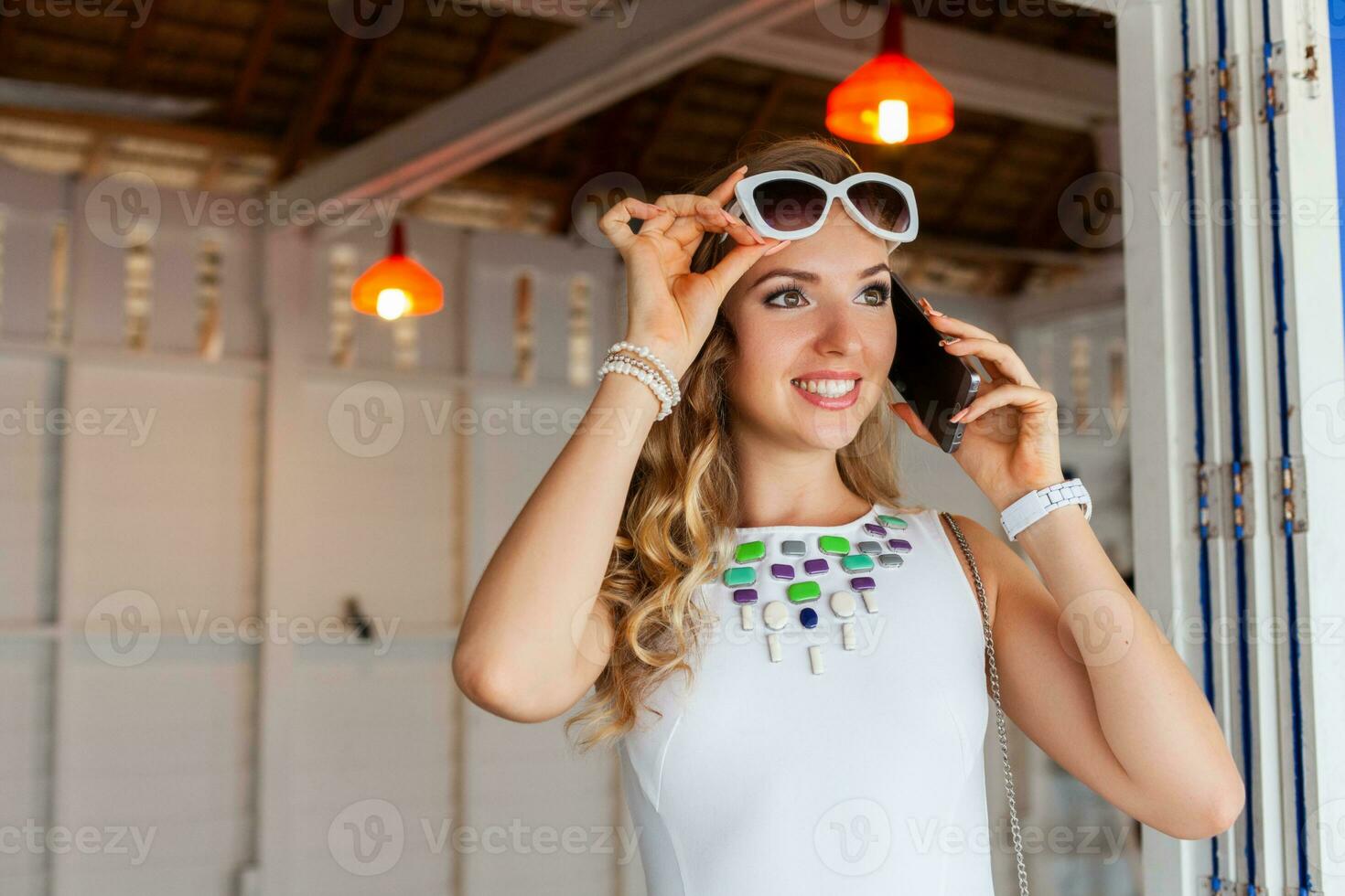 attractive woman in white dress in summer cafe in sunglasses talking on phone photo
