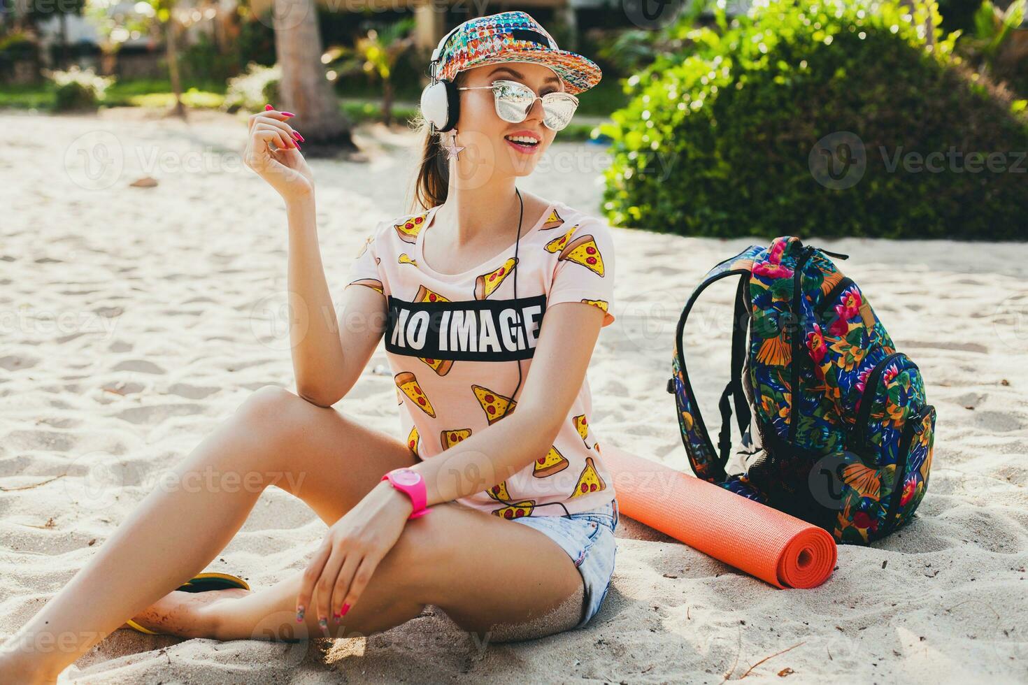 attractive hipster woman sitting on beach listening to music on headphones photo