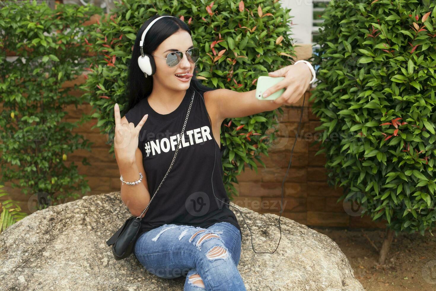 joven elegante hipster mujer en negro camiseta, vaqueros, escuchando a música en auriculares foto