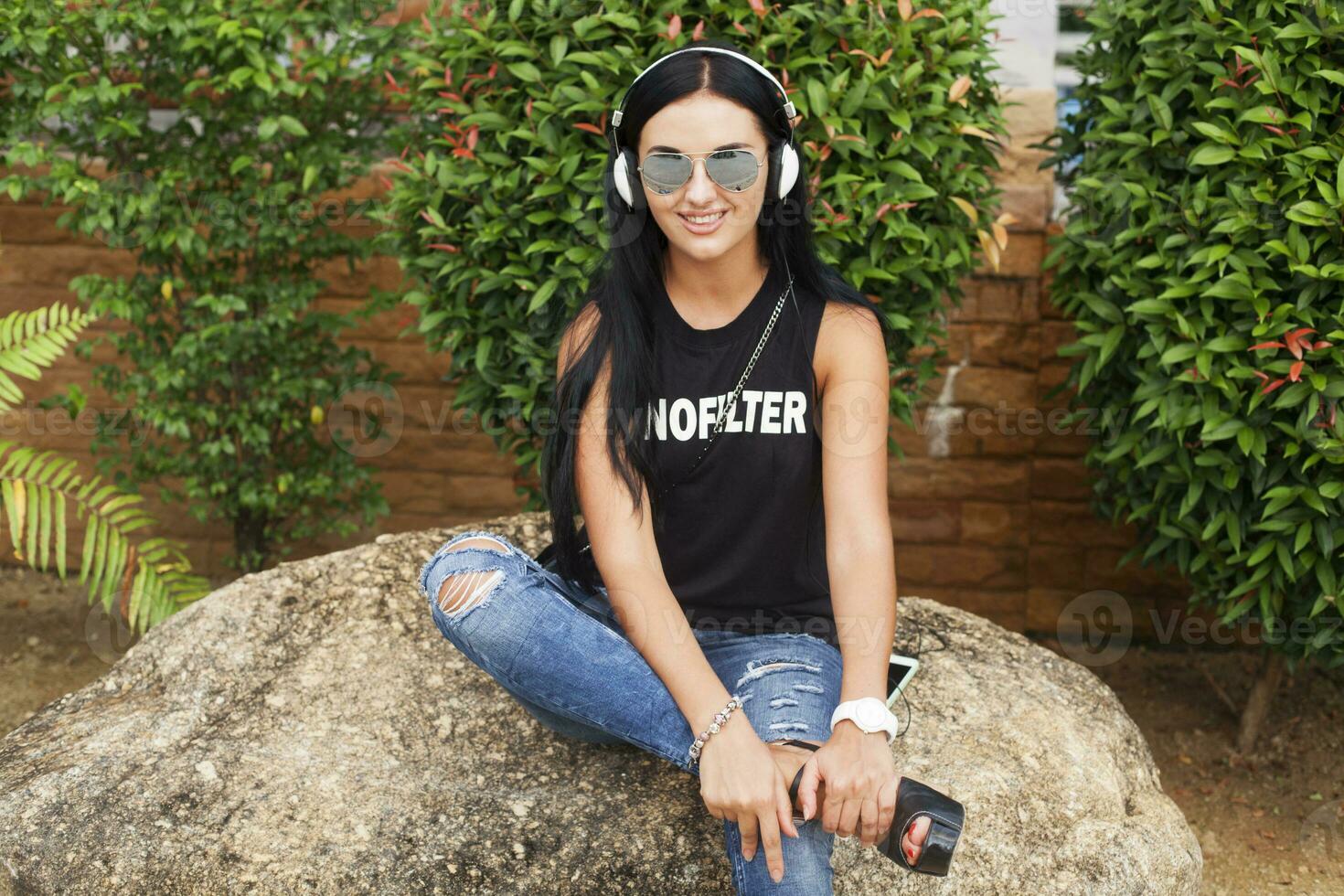 young stylish hipster woman in black t-shirt, jeans, listening to music on headphones photo