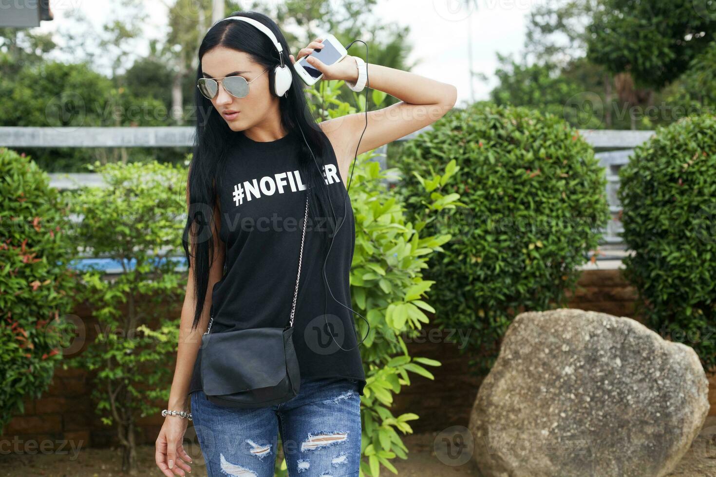 joven elegante hipster mujer en negro camiseta, vaqueros, escuchando a música en auriculares, teniendo divertido, posando, divertido, sonriente foto