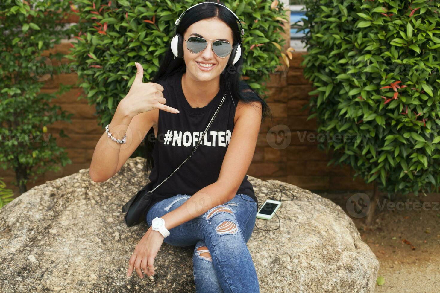 joven elegante hipster mujer en negro camiseta, vaqueros, escuchando a música en auriculares foto