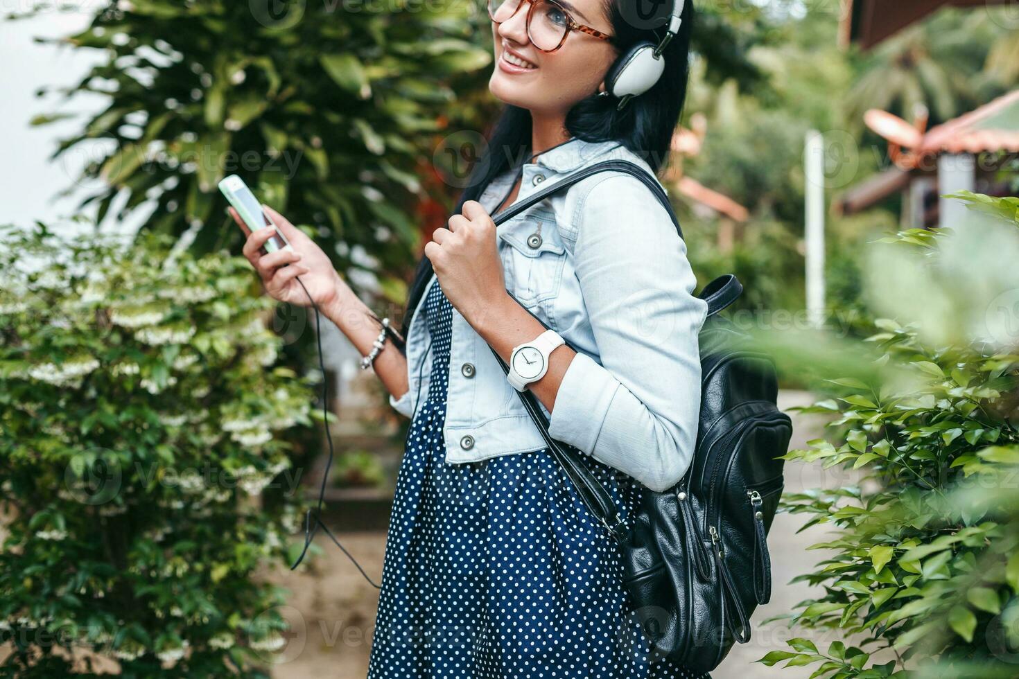 young stylish woman walking with smartphone, listening to music on headphones photo