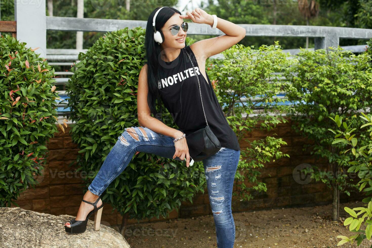young stylish hipster woman in black t-shirt, jeans, listening to music on headphones photo