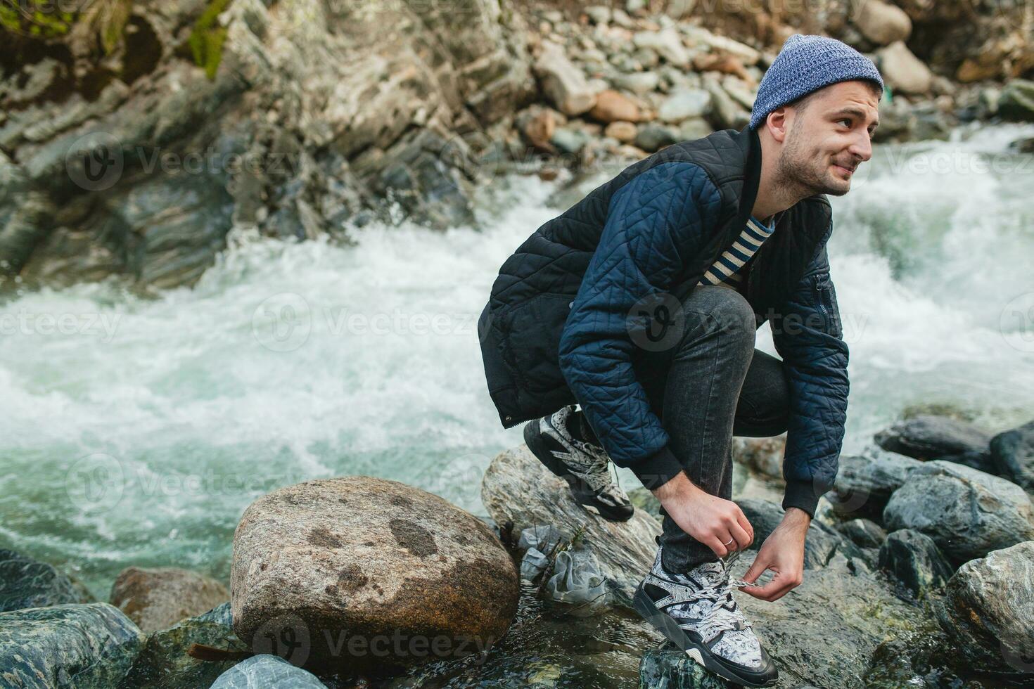 young hipster man walking on a rock at river in winter forest photo