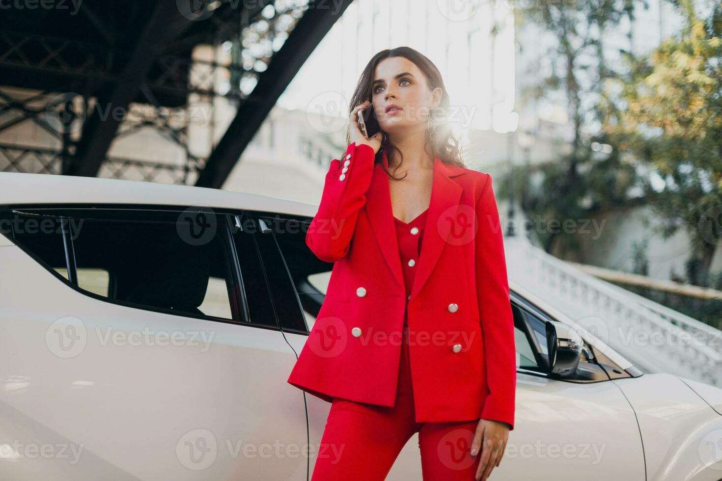 beautiful sexy woman in red suit posing at car talking on business on phone photo