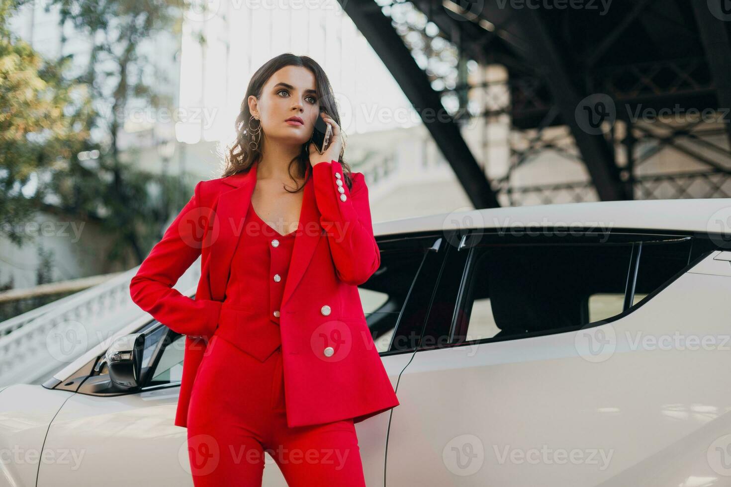 beautiful sexy woman in red suit posing at car talking on business on phone photo