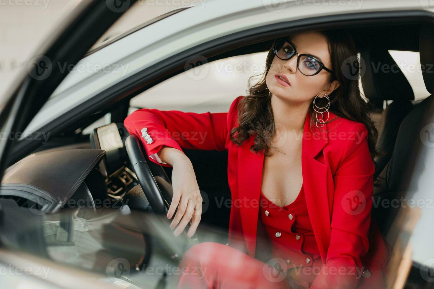 beautiful sexy rich business woman in red suit sitting in white car, wearing glasses photo
