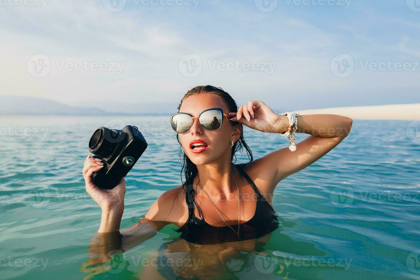 hermosa mujer, bronceado piel, negro bikini traje de baño, en pie en azul agua foto