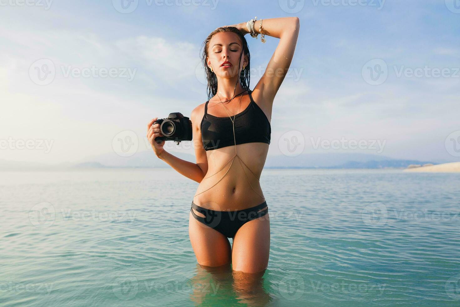 hermosa mujer, bronceado piel, negro bikini traje de baño, en pie en azul agua foto