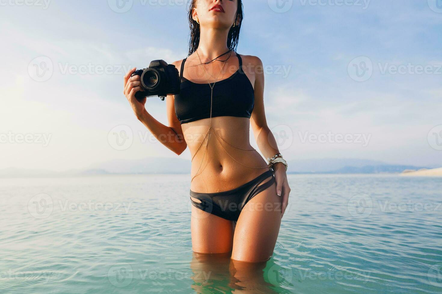 beautiful woman, tanned skin, black bikini swimsuit, standing in blue water photo