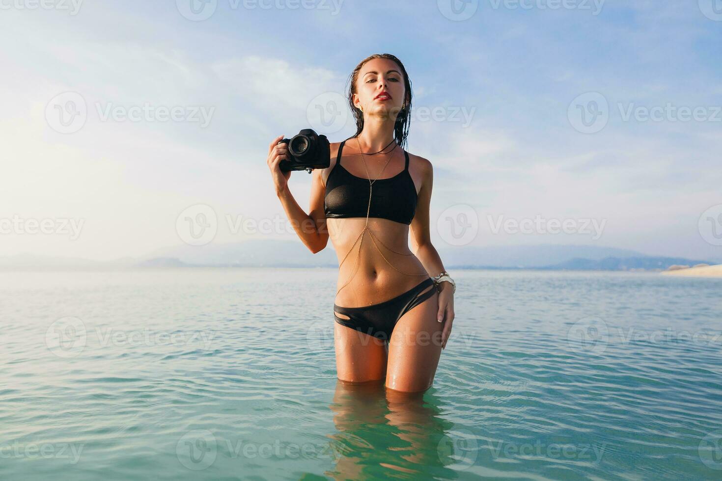 hermosa mujer, bronceado piel, negro bikini traje de baño, en pie en azul agua foto