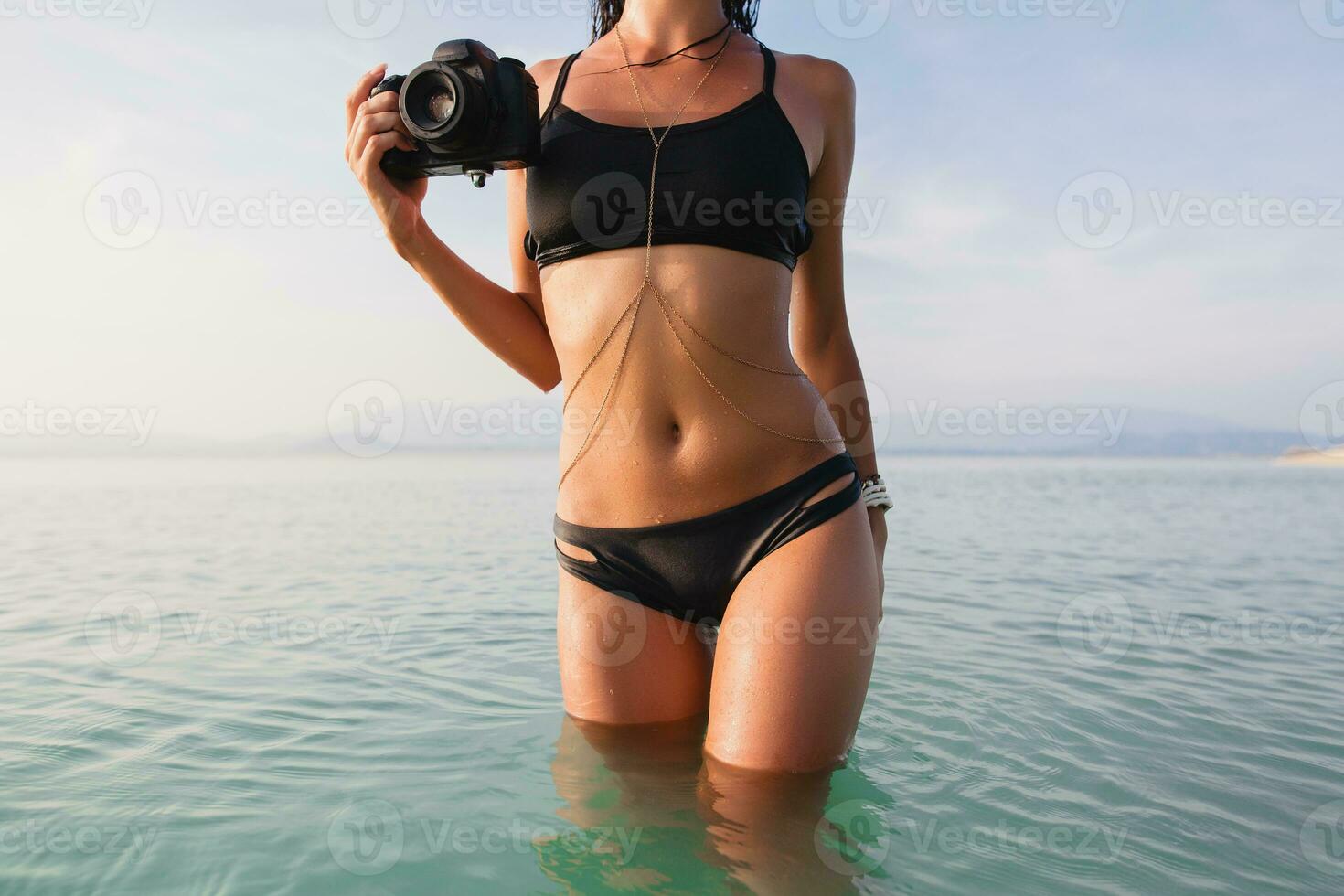 beautiful woman, tanned skin, black bikini swimsuit, standing in blue water photo