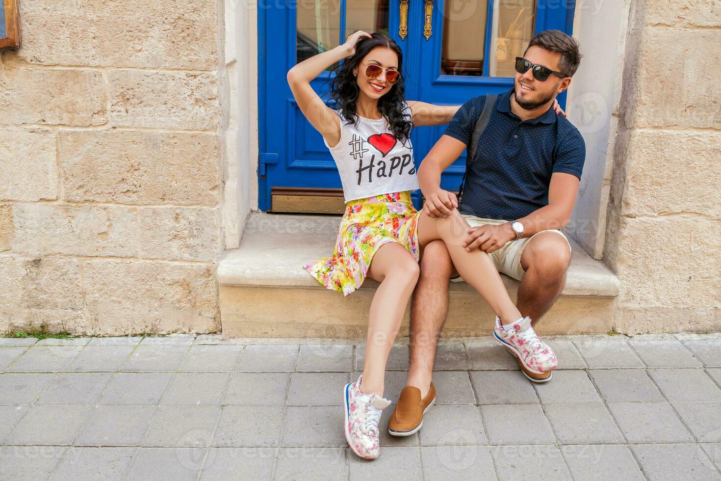young beautiful hipster couple in love sitting on old city street photo