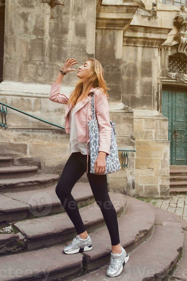 young beautiful woman traveling in europe, summer vacation, leather pink jacket, glam rock style, flirty, city street style photo