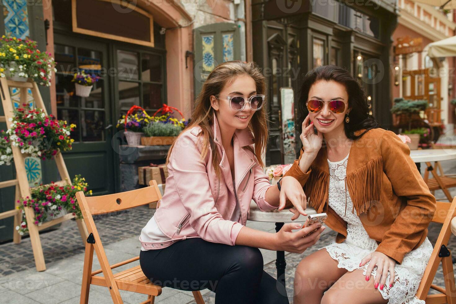 two young stylish women sitting at cafe, talking, gossiping, stylish trendy outfit photo