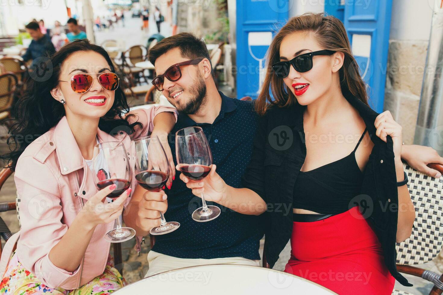 young hipster company of friends sitting in city street cafe, holding glasses photo