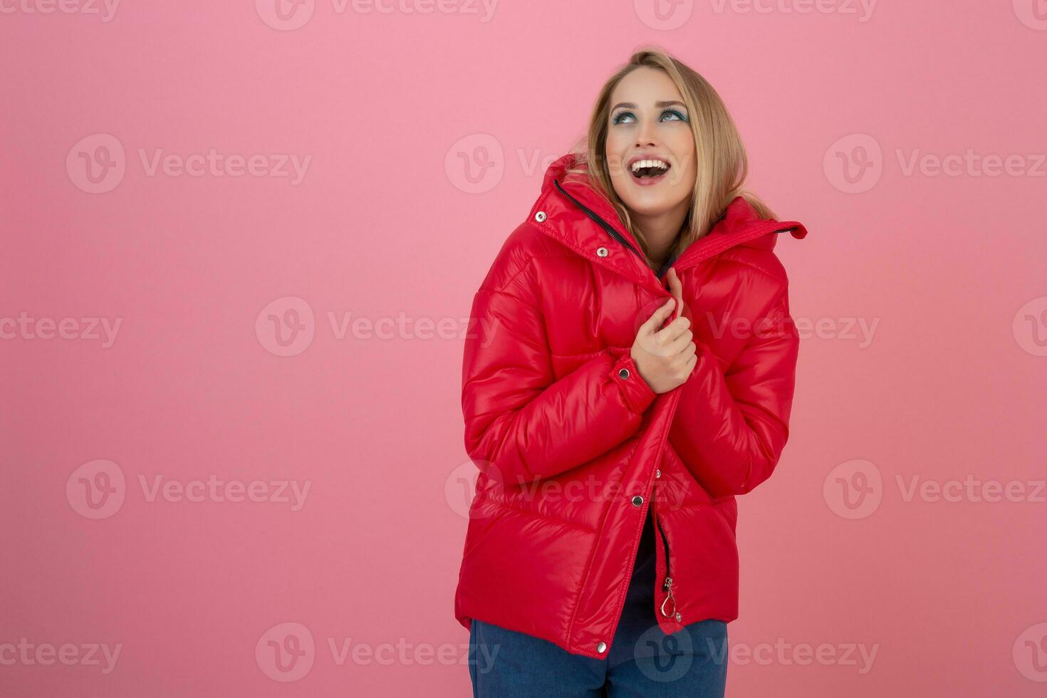 blond happy attractive active woman posing on pink background in colorful winter down jacket of red color, having fun, warm coat fashion trend, smiling photo