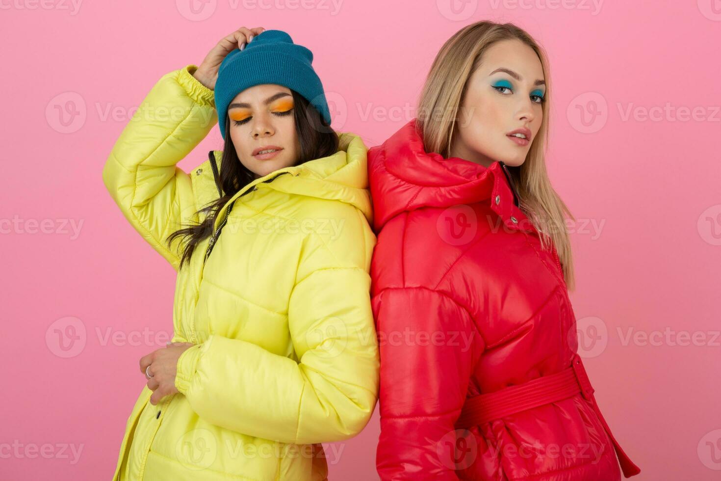 two attractive stylish women posing on pink background in colorful ...