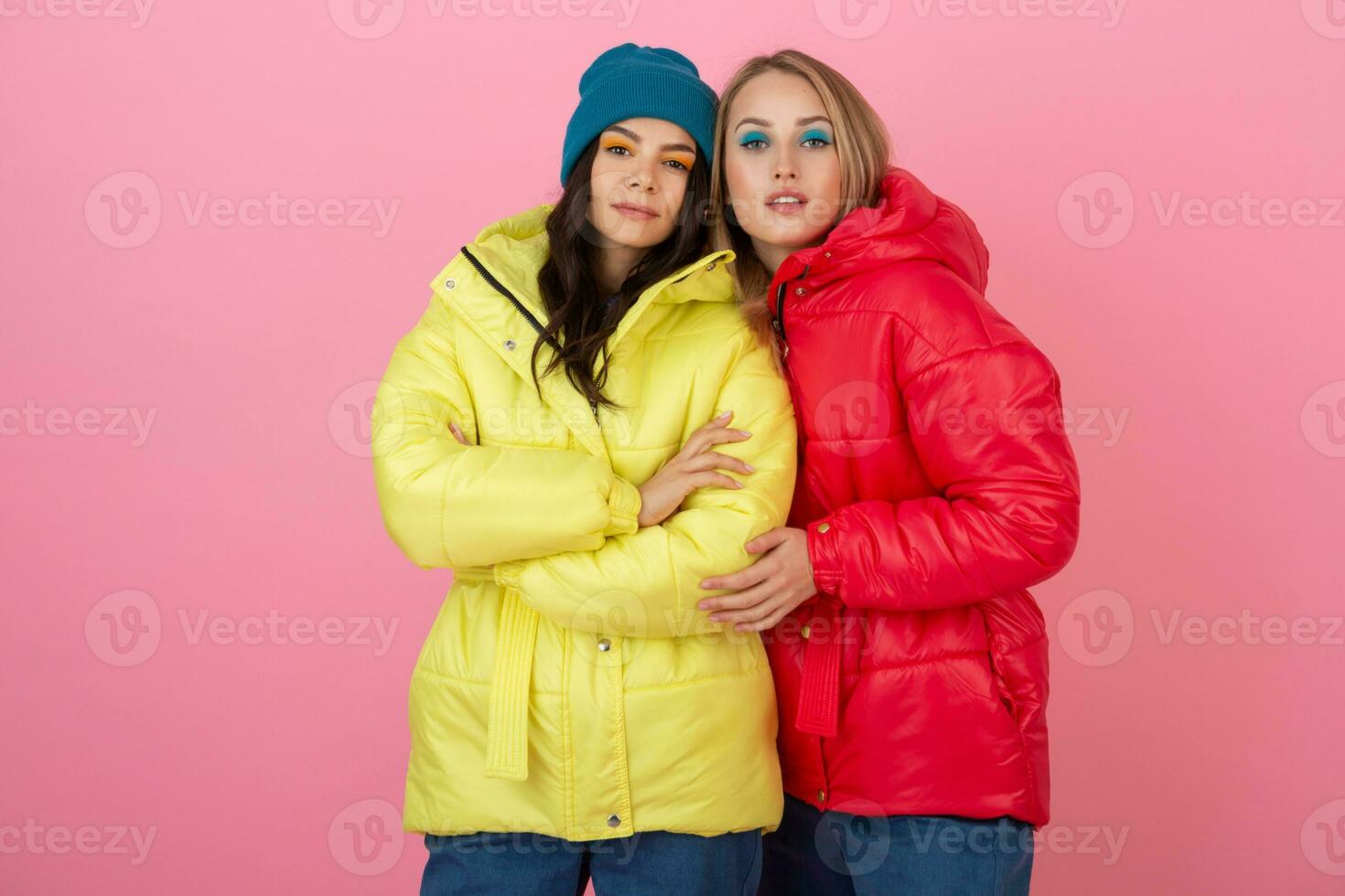 dos atractivo elegante mujer posando en rosado antecedentes en vistoso invierno abajo chaqueta de rojo y amarillo color, calentar ropa Moda tendencia foto