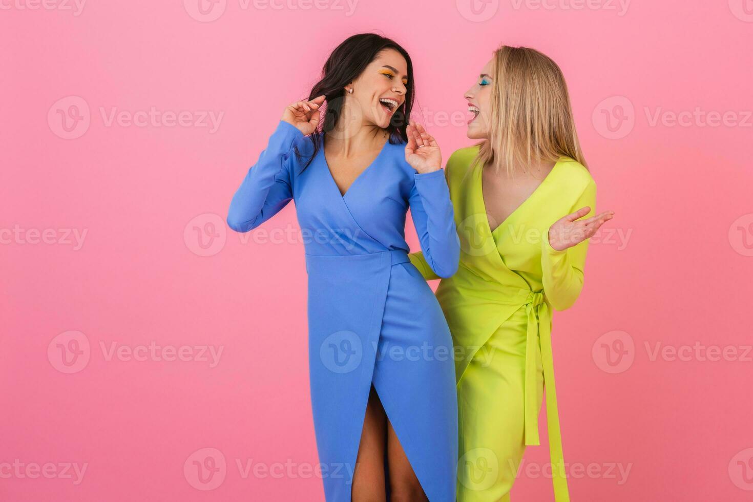 two stylish smiling attractive women having fun posing on pink background in stylish colorful dresses of blue and yellow color, spring fashion trend photo