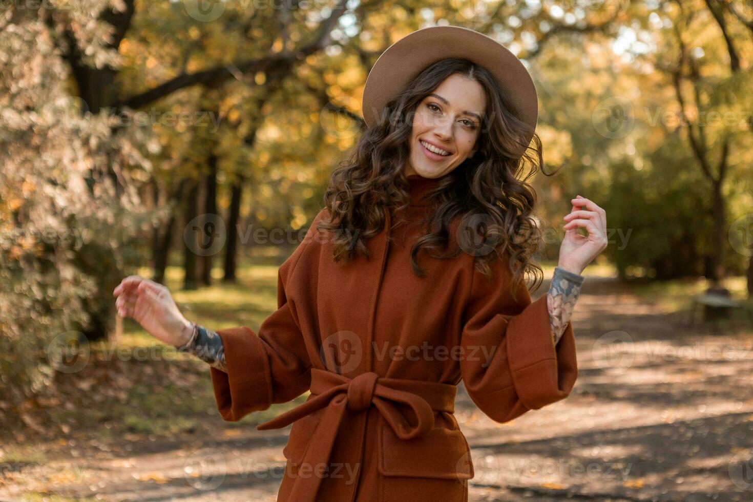 attractive stylish woman walking in park dressed in warm brown coat photo