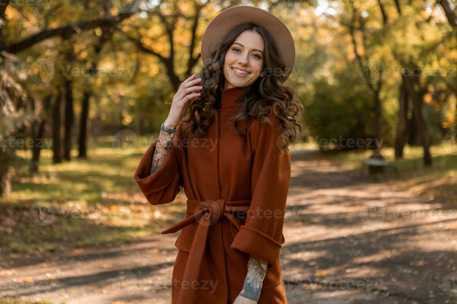 attractive stylish woman walking in park dressed in warm brown coat photo