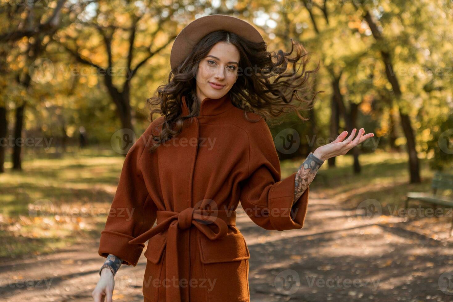attractive stylish woman walking in park dressed in warm brown coat photo