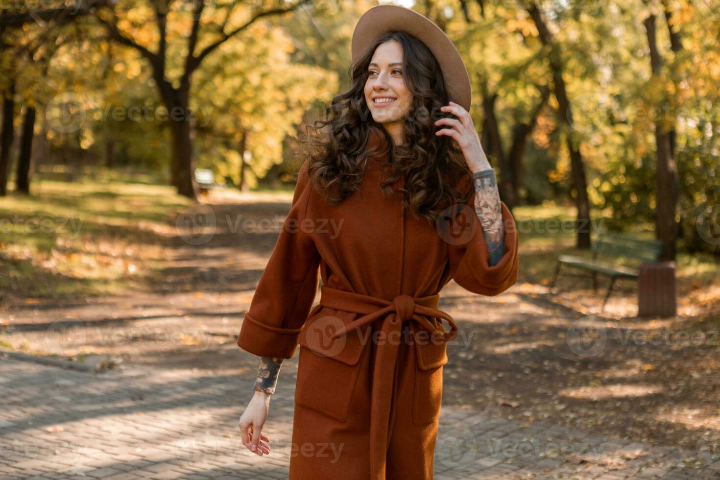 attractive stylish woman walking in park dressed in warm brown coat photo