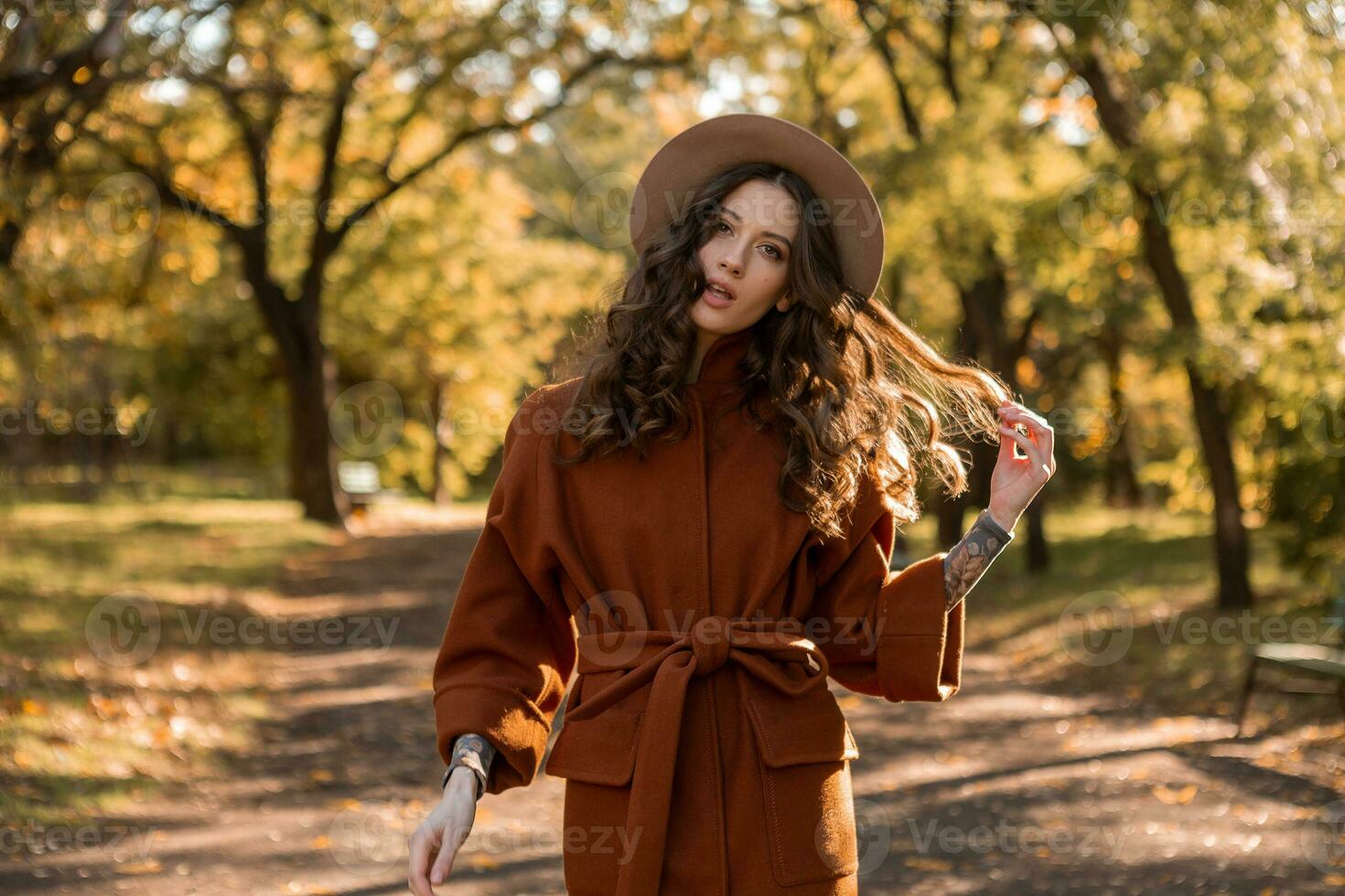 attractive stylish woman walking in park dressed in warm brown coat photo