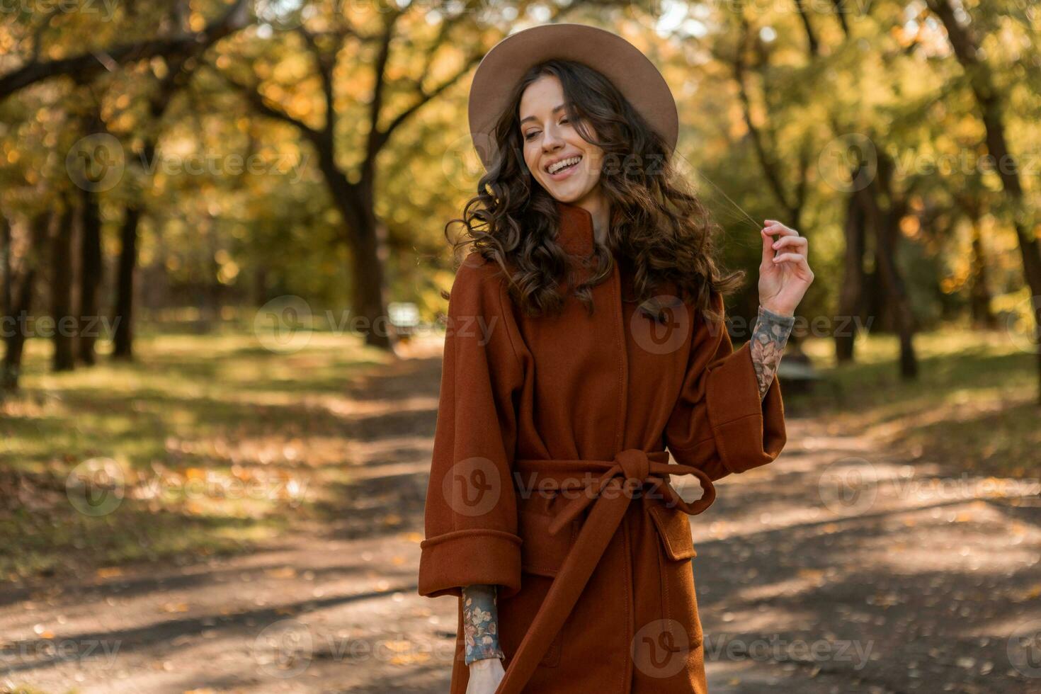 attractive stylish woman walking in park dressed in warm brown coat photo