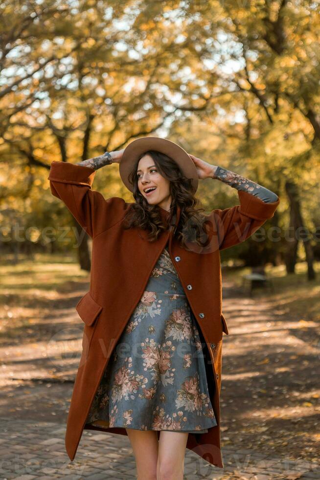 attractive stylish woman walking in park dressed in warm brown coat photo