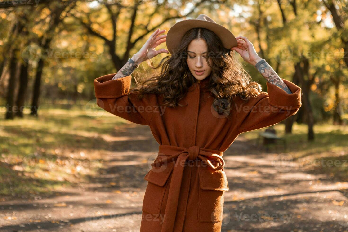attractive stylish woman walking in park dressed in warm brown coat photo