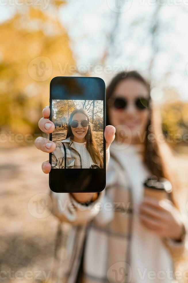 attractive young woman walking in autumn wearing jacket using phone photo