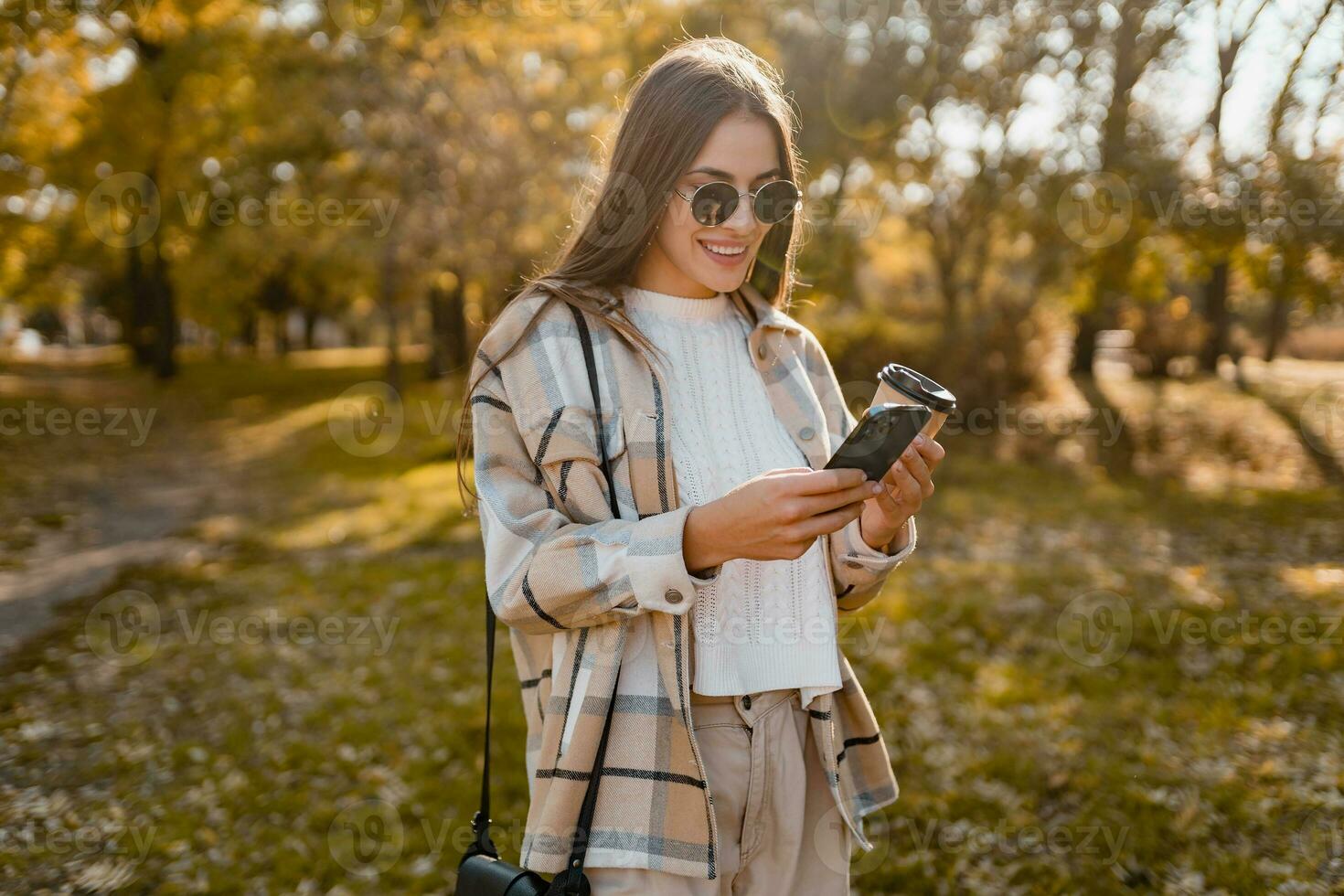 attractive young woman walking in autumn wearing jacket using phone photo