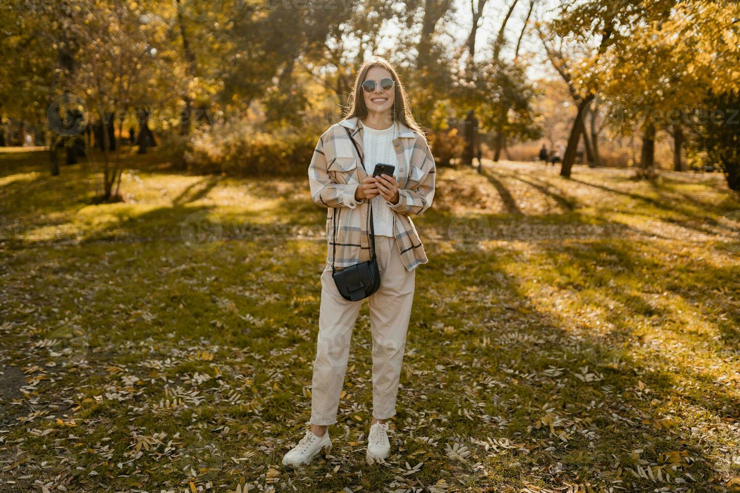 attractive young woman walking in autumn wearing jacket using phone photo