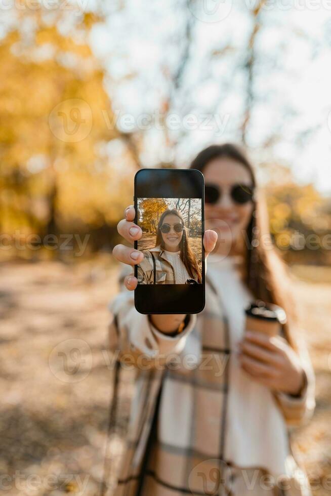 attractive young woman walking in autumn wearing jacket using phone photo