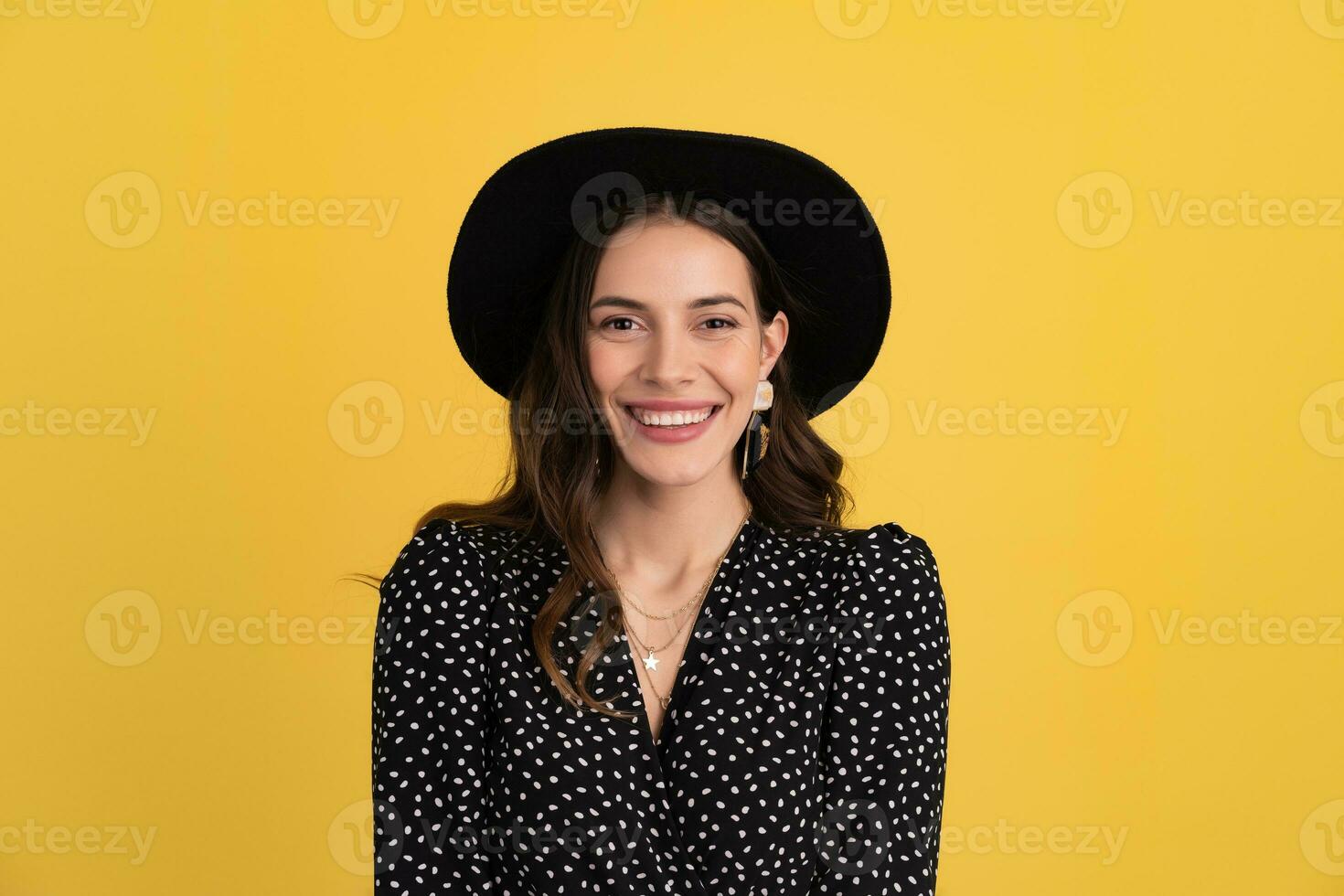 attractive woman posing isolated on yellow background wearing black hat and dress photo
