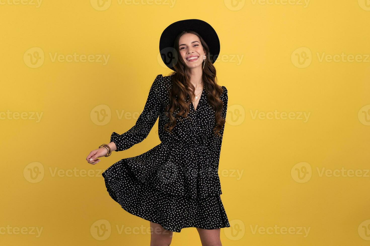 attractive woman posing isolated on yellow background wearing black hat and dress photo