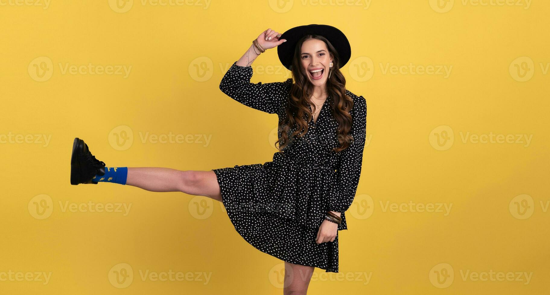 attractive woman posing isolated on yellow background wearing black hat and dress photo