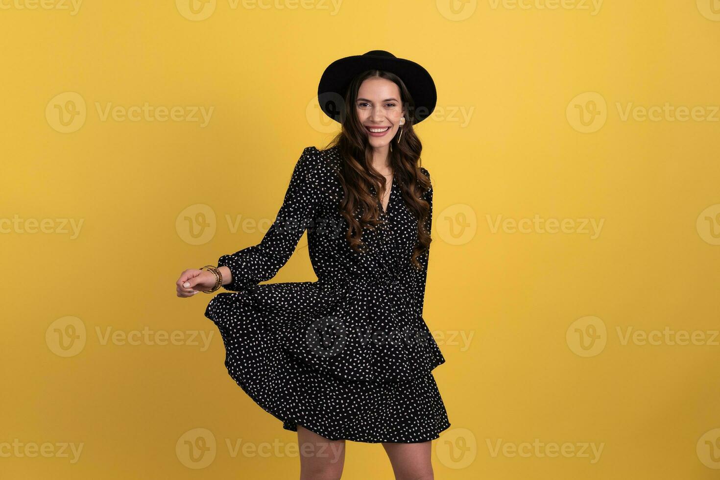 attractive woman posing isolated on yellow background wearing black hat and dress photo