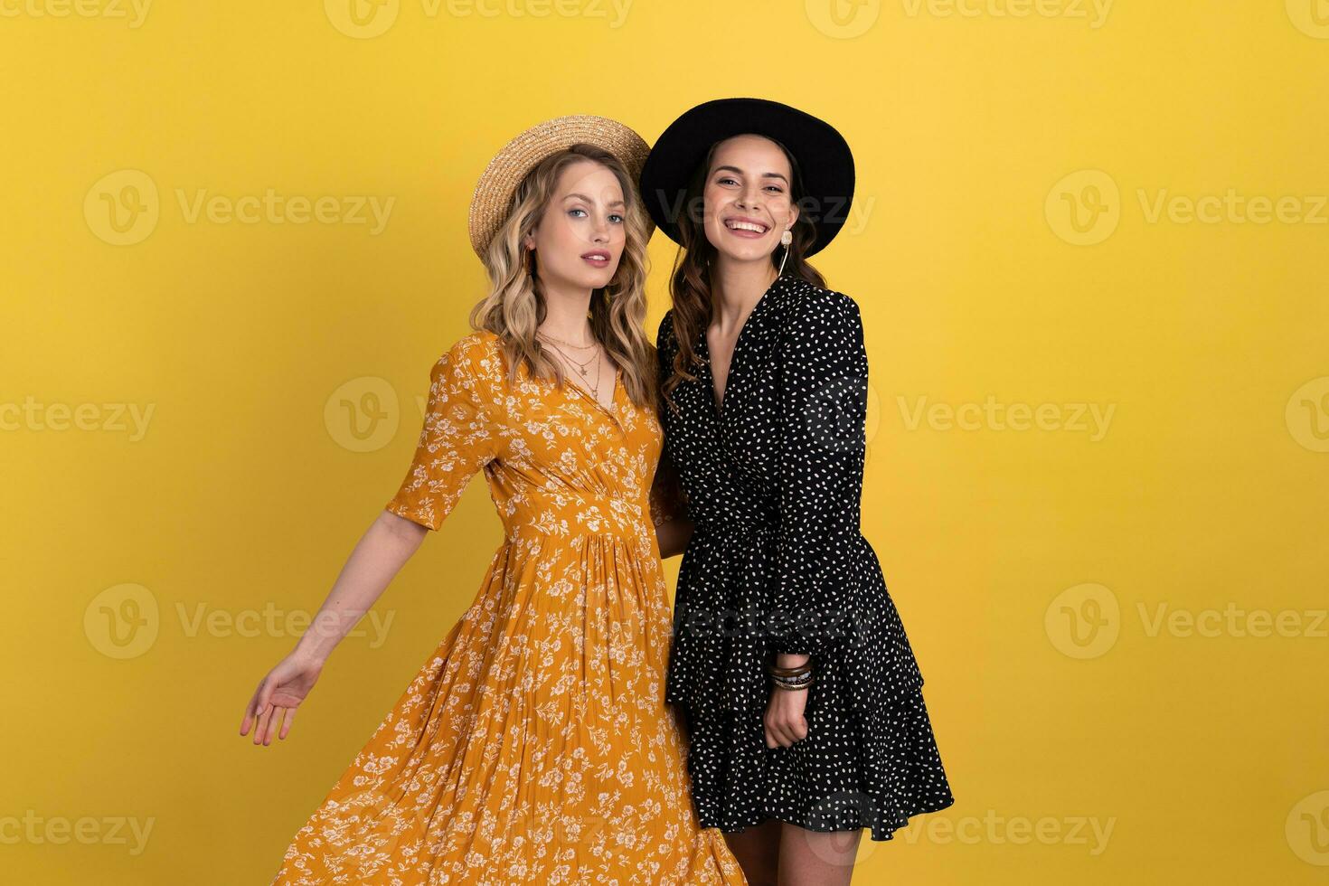 beautiful women friends together isolated on yellow background in black and yellow dress and hat photo