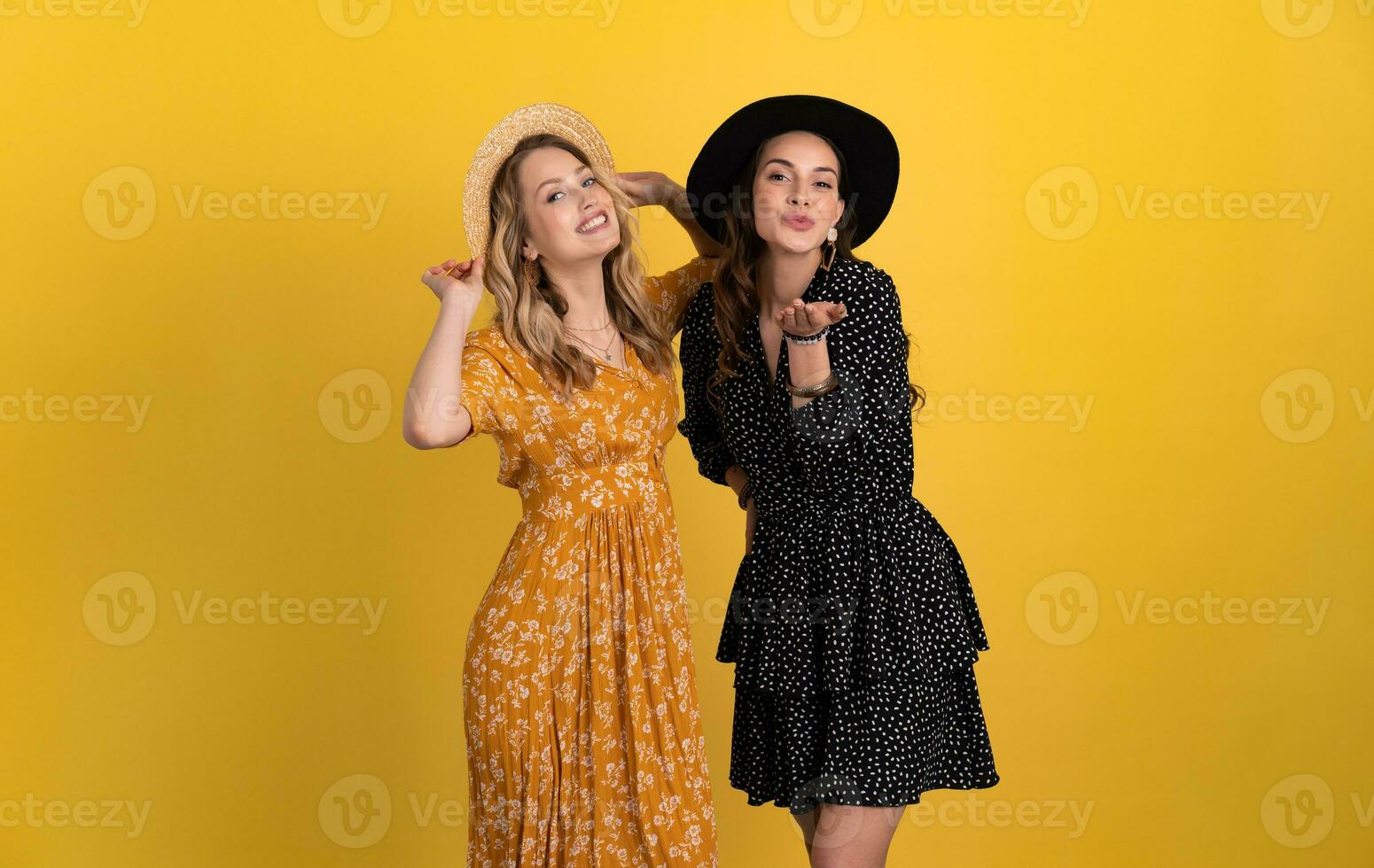 beautiful women friends together isolated on yellow background in black and yellow dress and hat photo