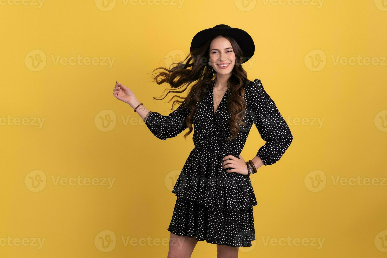 attractive woman posing isolated on yellow background wearing black hat and dress photo