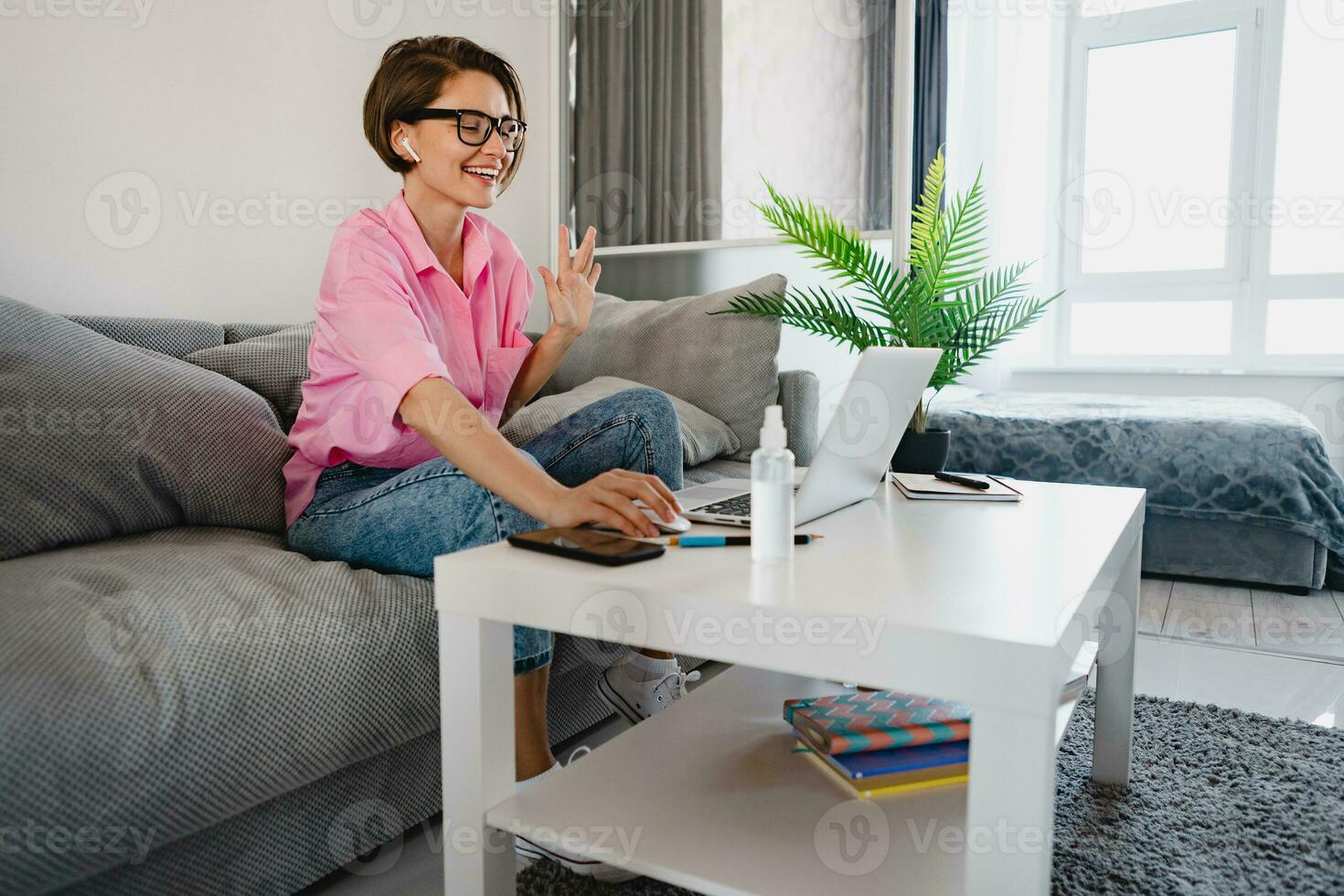 woman in pink shirt sitting relaxed on sofa at home at table working online on laptop photo